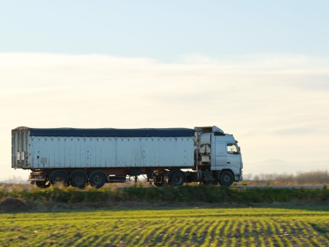 Semi-truck with tipping cargo trailer transporting sand from quarry driving on highway hauling goods in evening. Delivery transportation and logistics concept.