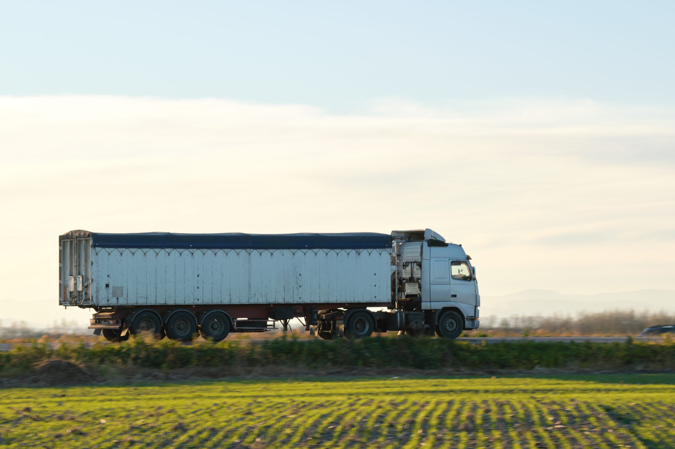 Semi-truck with tipping cargo trailer transporting sand from quarry driving on highway hauling goods in evening. Delivery transportation and logistics concept.